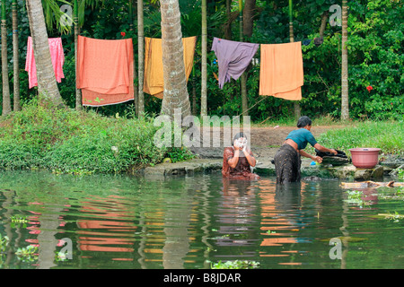 Auf den vielen Wasserkanälen von Kerala in den frühen Stunden des Morgens wäscht eine Frau ihre Kleider und andere wäscht sich Stockfoto