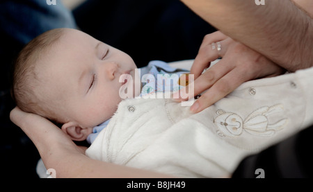 Ein schlafendes Baby Boy hat seinen schlafenden Anzug entfernt von seinem Vater und Großmutter ohne ihn wach. Stockfoto