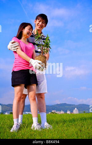 Junges Paar stehen auf dem Rasen eine Pflanze hält und glücklich lächelnd Stockfoto