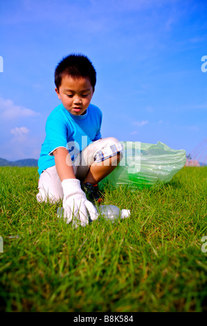 Kleiner Junge hob die leere Flasche und legt es in den Müllbeutel Stockfoto