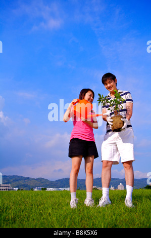 Junges Paar stehen auf dem Rasen hält einen kleinen Baum und Bewässerung Stockfoto