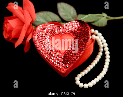 Ein Pailletten herzförmige Box mit einer Perlenkette im Inneren und eine rote Rose auf schwarz Stockfoto