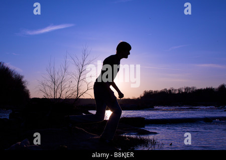 Mann läuft über Steinen bei Sonnenuntergang, auf dem James River in Richmond, Virginia. Stockfoto