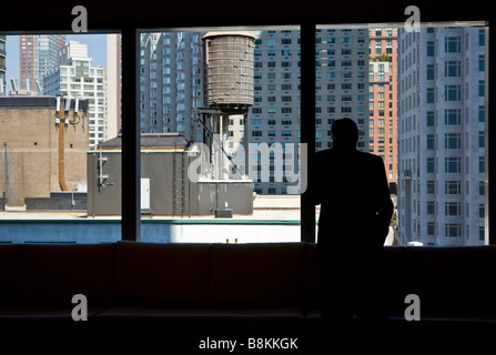 Ein Business-Mann steht Silhouette gegen eine Wand von Fenstern mit Blick auf Manhattan. Stockfoto