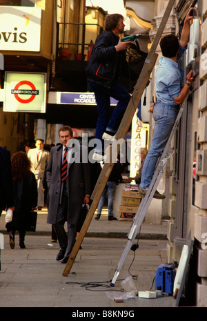 Piccadilly, London, Großbritannien, 1995: Installationsingenieure verwenden Leitern und Bohrer in Aufmachungen Beschilderung in der Nähe der u-Bahnstation Stockfoto