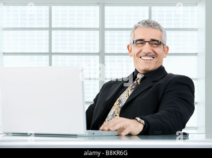 Glücklich reifer Geschäftsmann arbeiten auf Laptop-Computer am Schreibtisch az Büro lächelnd Stockfoto