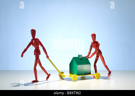 Zwei rote Mannequin Figuren bewegen ein grünen Musterhauses auf einem Wagen Stockfoto