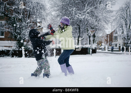 Zwei Kinder haben einen Schneeball an einem Winter-Morgen auf dem Weg zur Schule in London, Großbritannien zu kämpfen. Stockfoto