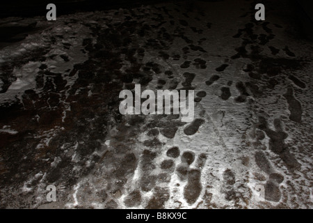 Fußspuren im Schnee und Eis auf Pflaster Beton in Dunkelheit Stockfoto