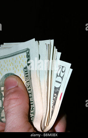 Daumen der linken Hand, die gefalteten USA zwanzig-Dollar-Scheine. Auf schwarz. Stockfoto
