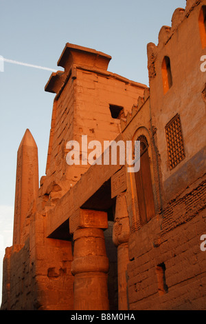 Ägypten, Luxor-Tempel-Ruinen, [niedrigen Winkel] Blick auf Obelisk, ersten Pylon und Wand der Moschee von orange Leuchten Sonnenuntergang beleuchtet Stockfoto