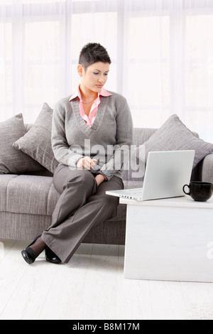 Junge Frau sitzt auf der Couch auf Laptop-Computer zu Hause arbeiten Stockfoto