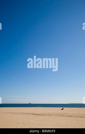 Sitzenden Person am Strand fliegt einen Drachen vor blauem Himmel. Stockfoto