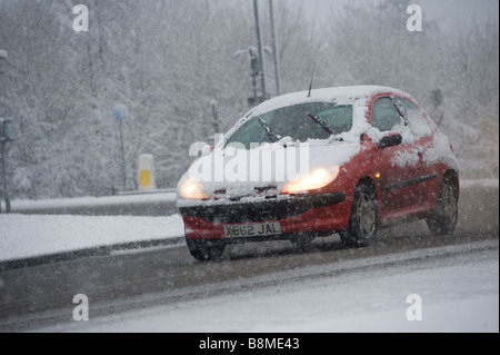 Auto fahren langsam auf einer verschneiten Straße im Winter in England mit Scheinwerfern mit Schnee bedeckt Stockfoto