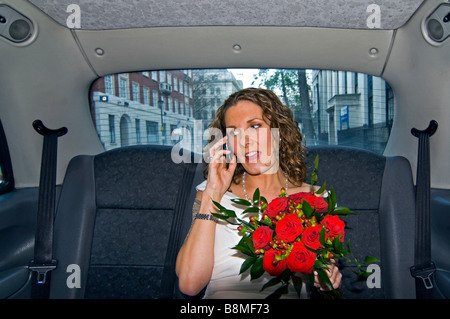 Humorvolle horizontale Porträt eine schöne Braut in einem traditionellen weißen Kleid auf ihrem Mobiltelefon in ein schwarzes Taxi sprechen. Stockfoto