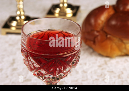 Ein Glas Wein für Schabbat mit Kerzen und Halla im Hintergrund Stockfoto