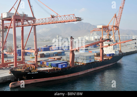 Boxschiff im Hafen von Fujairah am Golf von Oman, gestapelte Container auf dem Kai und Containerschiff neben einem bauchigen Bug Stockfoto