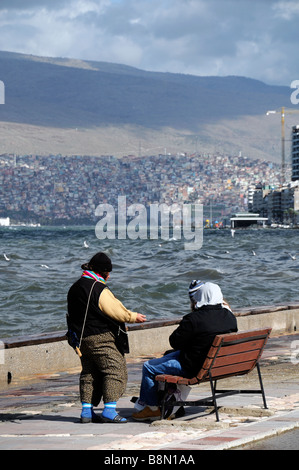 Paar sitzen sitzen auf einer Bank Gesicht Aussehen suchen zugewandten Ägäische Meer Golf von Izmir Türkei gesehen hinter einem Bettler Geld geben Stockfoto