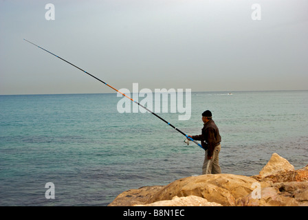 Einsamen Fischer angeln Mittelmeer Seawall Promenade Wellenbrecher mit langen Surf Rute und spinning reel Stockfoto