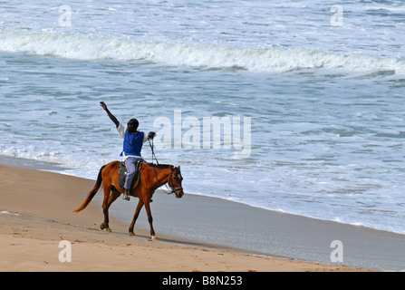 Mann auf Reiten Wellen für weibliche Touristen am Strand, The Gambia "West Afrika" Stockfoto