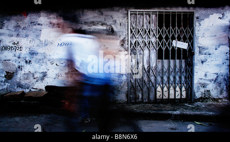 Ein Mann schafft eine Unschärfe, wie er vorbei an einer grob gemalte Wand in einer Wohnstraße in Guangzhou, China geht. Stockfoto