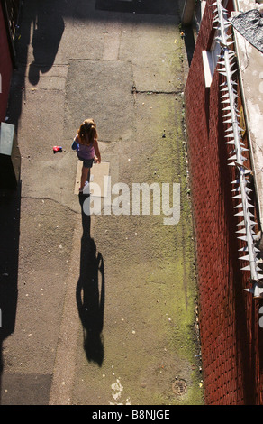 Ein junges Mädchen zu Fuß durch eine Wohnsiedlung mit einem Sicherheitszaun zu ihrer Rechten an einem Sommernachmittag. Stockfoto