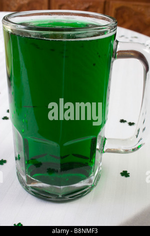 Ein Glas grünes Bier mit Kleeblatt Konfetti auf einer weißen Tischdecke Stockfoto