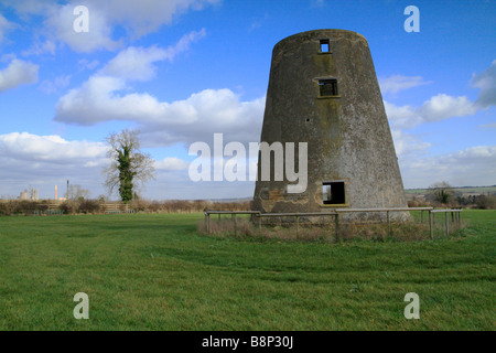 Ein zerstörte, verlassenen Windmühle Turm auf einem Hügel, mit einem modernen Zement arbeitet in Thedistant Hintergrund Stockfoto