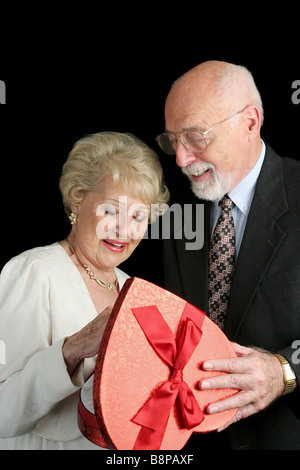 Ein hübscher senior Mann seine schöne Frau und eine Schachtel mit Valentine Schokolade verleiht schwarzen Hintergrund Stockfoto