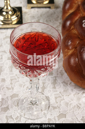 Eine Nahaufnahme Foto von einem Glas Wein für Schabbat mit Challah Brot und Kerzen im Hintergrund Stockfoto