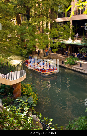 San Antonio River Walk Riverwalk Tourenboot mit Touristen Pässe neben Straßencafés und Bäume mit leuchtend grünen Blättern Stockfoto