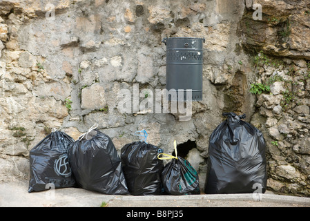 Mehrere Taschen von Müll aufgereiht entlang Steinmauer unter montierten Mülleimer Stockfoto