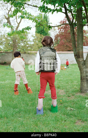 Kleine Mädchen mit Kunststoff-Eimer als Stelzen, Rückansicht Stockfoto