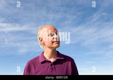 Ein Mann mittleren Alters steht gegen den blauen Himmel, die Wärme der Sonne im Gesicht. Stockfoto