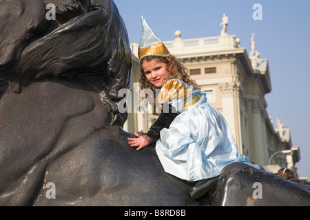 Junges Mädchen verkleidet in Kostüm für Fasching auf eine Löwenstatue sitzen. Stockfoto