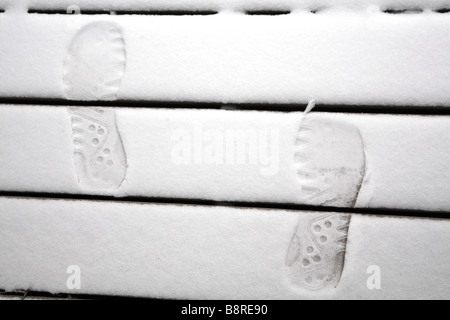 Fußspuren im Schnee auf Holzstufen. Stockfoto