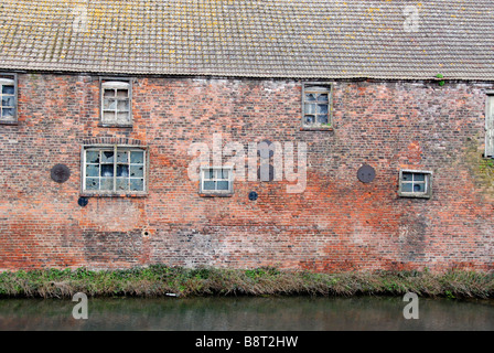 Kaputte Fenster, geben Sie verblasste Lackierung und Rasen an der Basis ein verlassenes Gebäude am Fluss Stockfoto