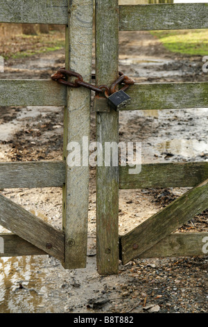 Verschlossene Tore, Holztor, gesichert, rostiger Block-Verschluss, Kette, Farm Track, rostiger Block-Lock, Schlamm auf der Straße, Farm Tore, ländlich, Stecken im Schlamm, Bauern, Traktor. Stockfoto