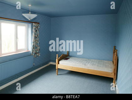 Eine leere blaue Schlafzimmer mit 1970 Stil Artex Wänden und einem leeren Bett in der Ecke Stockfoto
