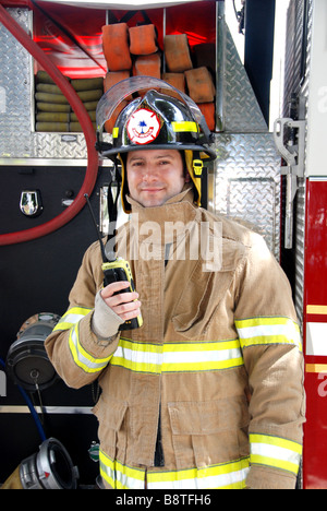 Lächelnde männlichen Feuerwehrmann hält Radio vor Feuerwehrauto Bunker Ausrüstung und Helm tragen Stockfoto