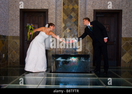 Eine Braut und Bräutigam miteinander erreichen und berühren über eine Wasserfontäne am Tag ihrer Hochzeit. Stockfoto