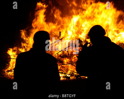 Zwei Männer, die Silhouette vor ein riesiges Feuer Feuer aus der Verbrennung von alten Weihnachtsbäume Stockfoto