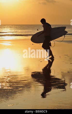 Reflexion der Surfer mit Surfbrett am Strand entlang am Sonnenuntergang, Strand von Kuta, Bali, Indonesien. Stockfoto