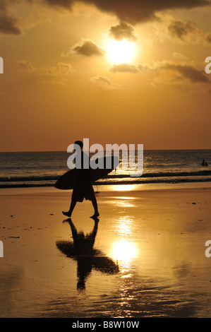 Surfer mit Surfbrett am Strand entlang am Sonnenuntergang, Strand von Kuta, Bali, Indonesien. Stockfoto