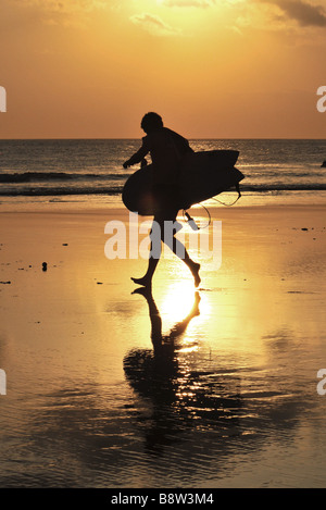 Surfer mit Surfbrett am Strand entlang am Sonnenuntergang, Strand von Kuta, Bali, Indonesien. Stockfoto