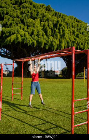 Junge Frau hängt an einer horizontalen Leiter in Honomu, Big Island, Hawaii, USA Stockfoto