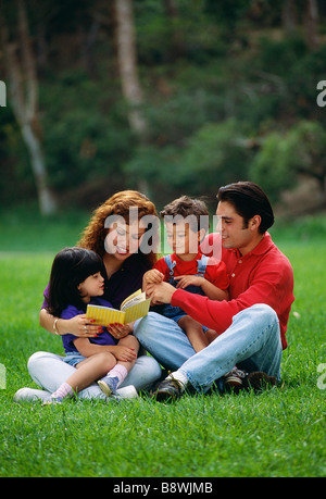 Latino oder hispanischen Familie, Mutter und Vater mit Sohn und Tochter sitzen und lesen gemeinsam draußen in einem Park. Stockfoto