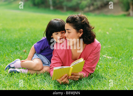 Latina-Mutter und Tochter ein Buch draußen auf dem Rasen. Stockfoto