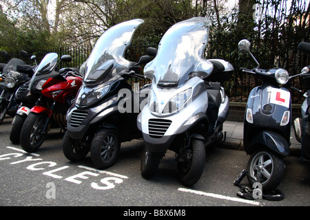 Motorräder, darunter zwei Piaggio MP3, Dreiräder mit zwei Vorderrädern, geparkt in St James Square, London. Stockfoto