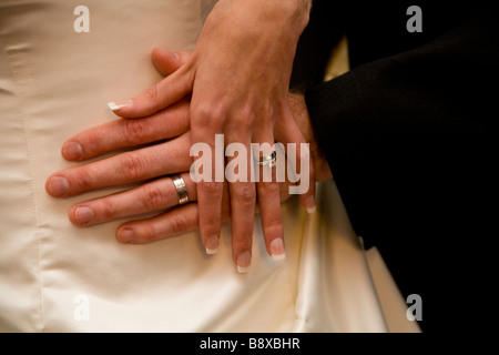 Nahaufnahme von Braut und Bräutigam, die ihre Eheringe gegen das Brautkleid zeigen. Stockfoto